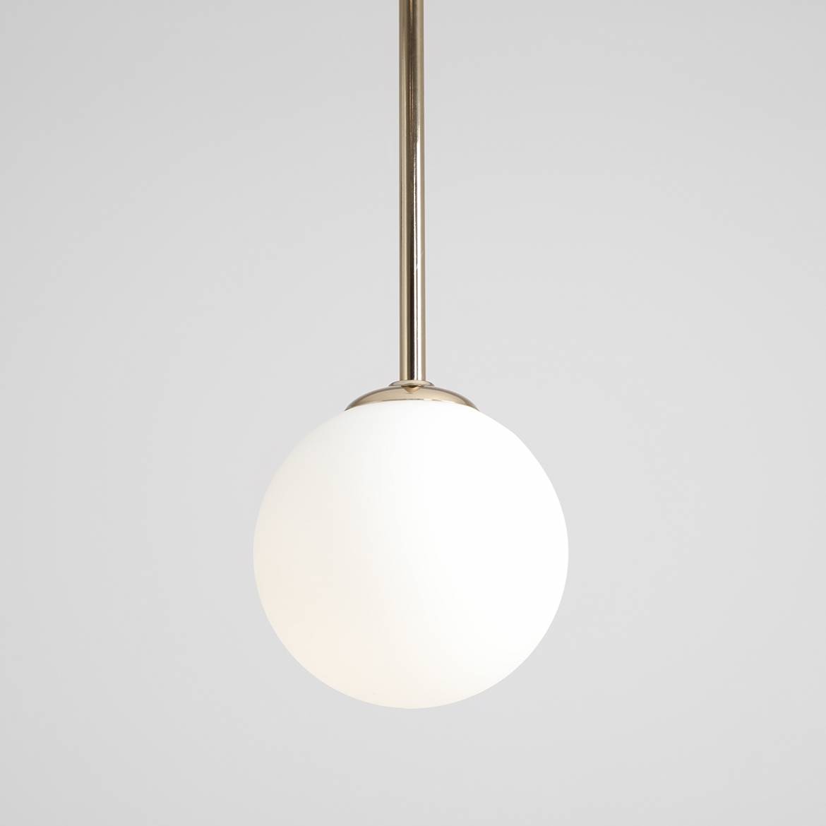 Lampa wisząca Bosso D14 o złotym wykończeniu z białym, okrągłym kloszem. Ujęcie frontalne, lampa zawieszona na cienkim pręcie. Prosty design, idealna do nowoczesnych wnętrz. Tło w jednolitej, jasnej kolorystyce.