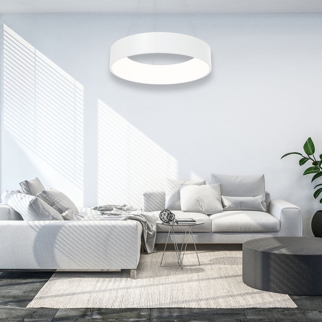 Biała lampa wisząca Ohio LED o okrągłym kształcie, zawieszona nad nowoczesnym, jasnym wnętrzem. Lampa emituje równomierne światło, a w tle widoczna jest szara sofa, stół kawowy oraz roślina doniczkowa.