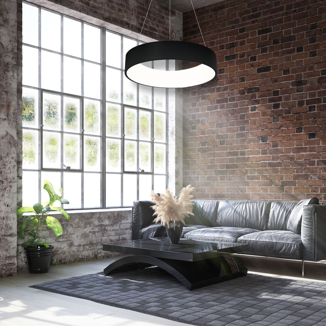 Czarna lampa wisząca Ohio LED o okrągłym kształcie, zawieszona na cienkich linkach, emituje jasne światło. Znajduje się w nowoczesnym salonie z ceglaną ścianą, skórzanym sofą i dekoracyjnymi roślinami w doniczkach.