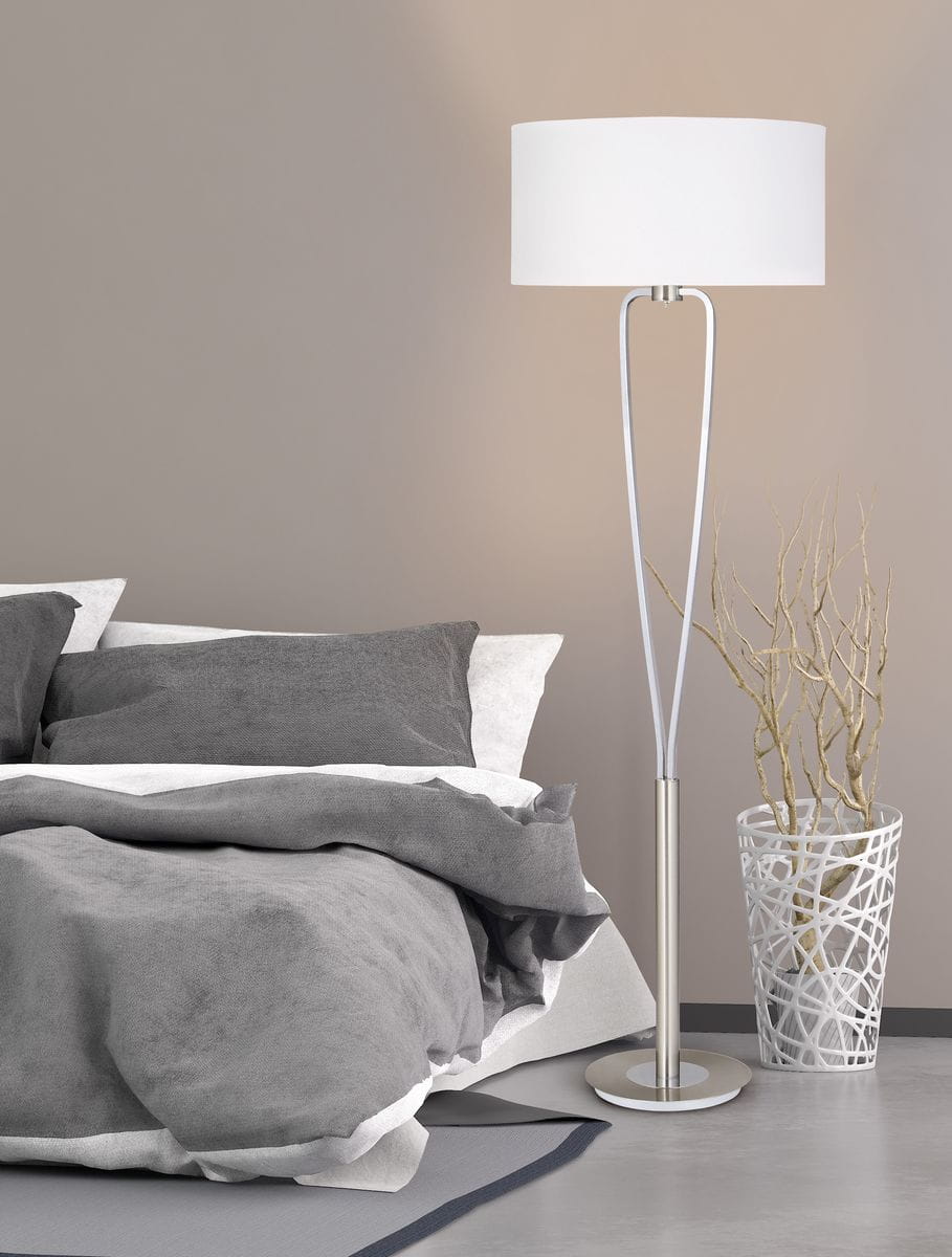 Lampa podłogowa Paris II w kolorze niklowym z białym kloszem o okrągłym kształcie, stojąca na okrągłej podstawie. Ujęcie z boku, w kontekście sypialni z pościelą w odcieniach szarości i dekoracyjną donicą obok.