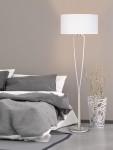 Lampa podłogowa Paris II w kolorze niklowym z białym kloszem o okrągłym kształcie, stojąca na okrągłej podstawie. Ujęcie z boku, w kontekście sypialni z pościelą w odcieniach szarości i dekoracyjną donicą obok.