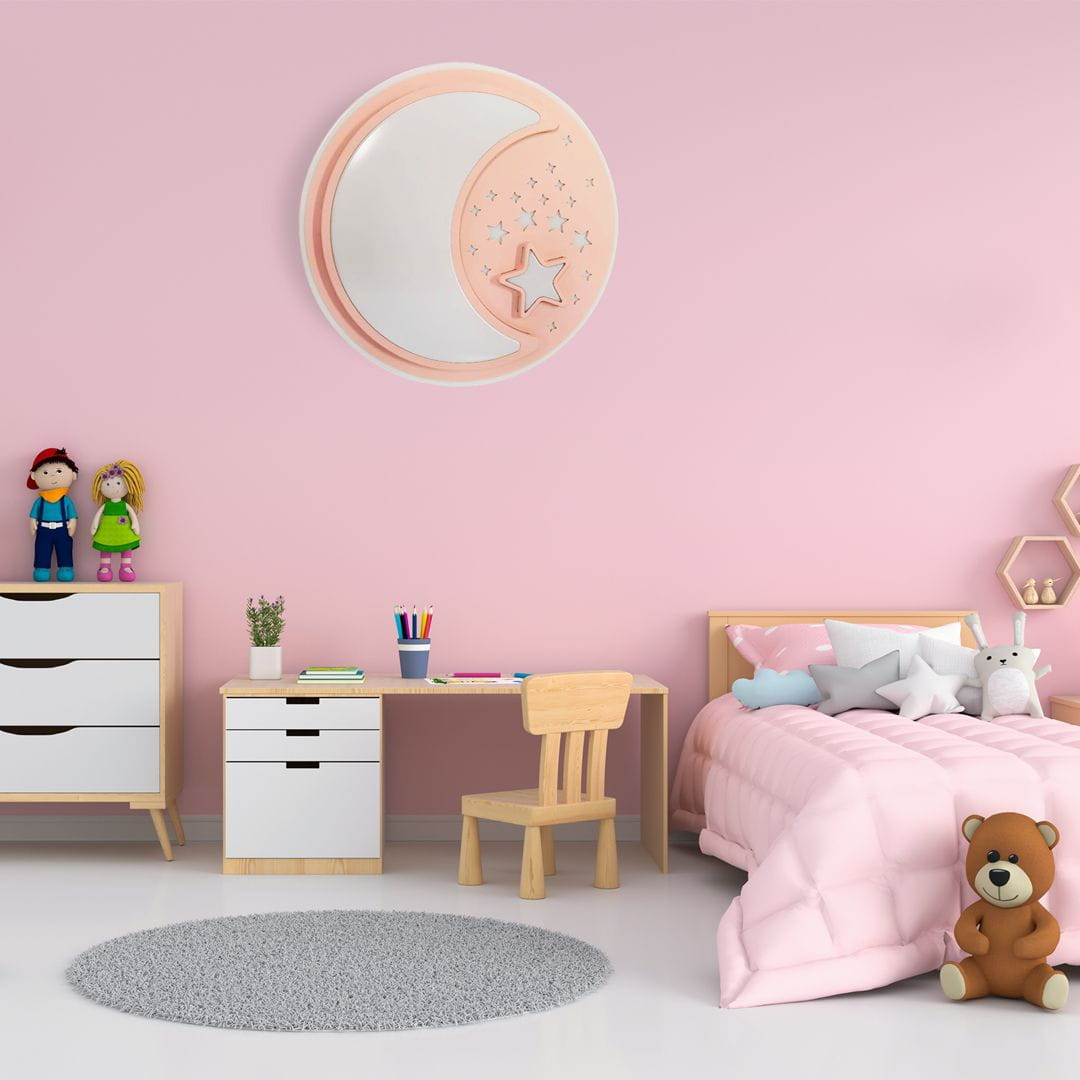 Plafon LED Note Pink w kształcie półksiężyca i gwiazdy, z możliwością regulacji kolorów 3000-6000K, zawieszony na różowej ścianie. W otoczeniu mebli dziecięcych, w tym biurka, krzesła i dekoracji, tworzy przytulny klimat.