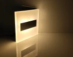 Lumi White LED oprawa schodowa 230V, ciepła barwa 3000K, z matowym białym korpusem i czarnym panelem. Ujęcie z boku, oprawa lekko podświetlona, z odbiciem na powierzchni. Idealna do oświetlenia schodów lub korytarzy.
