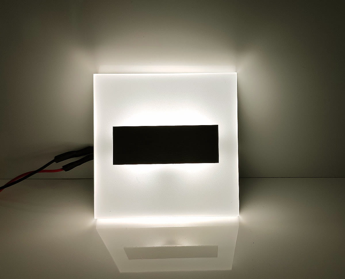 Oprawa schodowa Lumi White LED 230V w barwie neutralnej 4000K, prostokątna, z mlecznym szkłem i czarnym akcentem w centralnej części. Wykonana z materiałów wysokiej jakości, podświetlana z tyłu, leżąca na gładkiej powierzchni.