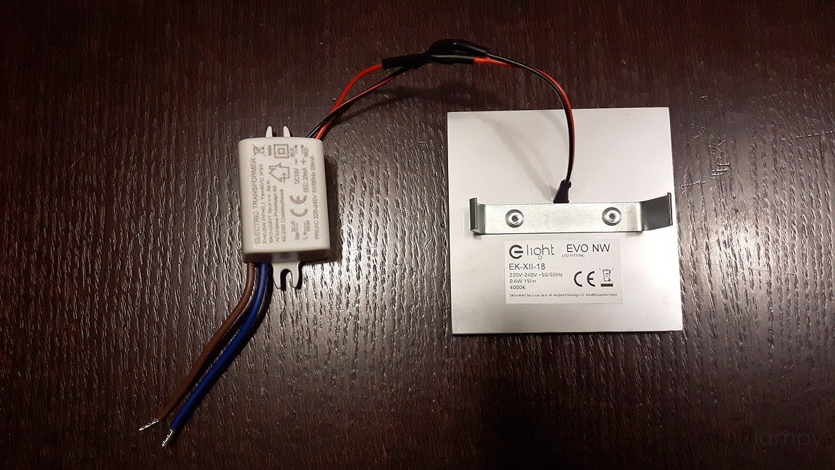 Evo Black LED oprawa schodowa 230V z neutralną barwą 4000K. Prosta, kwadratowa obudowa z metalowym mocowaniem, widoczny zasilacz z przewodami w kolorach brązowym, niebieskim i czarnym. Ujęcie frontalne, produkt na ciemnym tle.