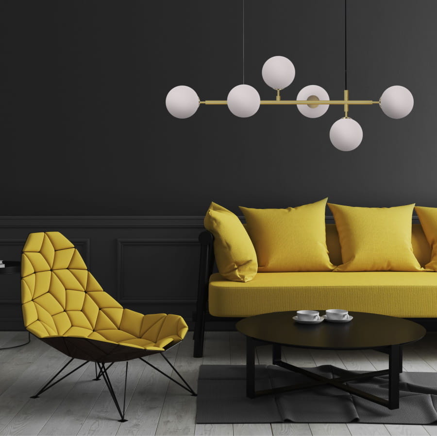Lampa wisząca Alisa 6-punktowa w kolorze mosiądzu i białym z kloszami w kształcie kul, zawieszona nad żółtą sofą. Widok z przodu, eksponujący elegancki design i nowoczesny styl w minimalistycznej aranżacji.