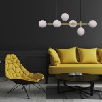 Lampa wisząca Alisa 6-punktowa w kolorze mosiądzu i białym z kloszami w kształcie kul, zawieszona nad żółtą sofą. Widok z przodu, eksponujący elegancki design i nowoczesny styl w minimalistycznej aranżacji.