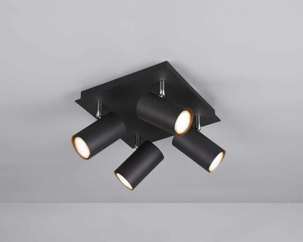 Czarna lampa sufitowa typu spot z czterema cylindrycznymi reflektorami, zamocowana na kwadratowej podstawie. Reflektory mają złote detale wewnętrzne i są ustawione pod różnymi kątami, co pozwala na regulację kierunku światła.
