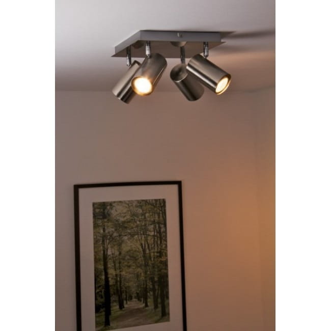Lampa sufitowa Marley 4-punktowa w kolorze niklowym. Składa się z czterech metalowych reflektorów, zamocowanych na kwadratowej podstawie. Ujęcie z góry, na tle ściany z ramką i obrazem przedstawiającym las.