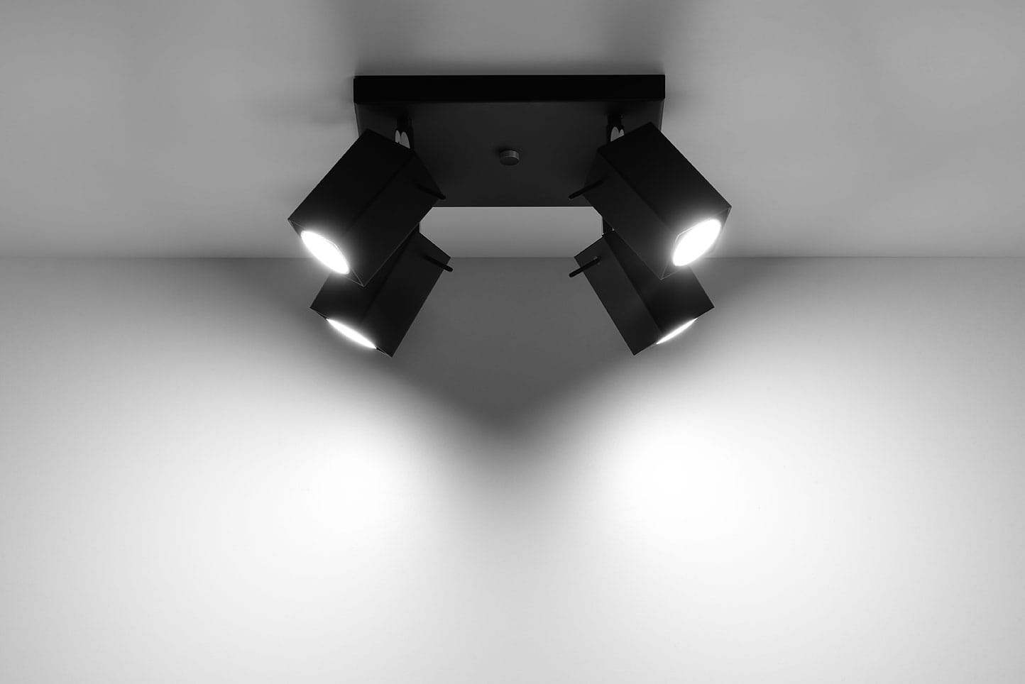 Czarna lampa sufitowa Merida, 4-punktowa, z kwadratowym metalowym stelażem. Lampy w formie prostokątnych reflektorów, skierowane w różne strony, montowane na suficie. Tło białe, minimalistyczne, podkreślające nowoczesny design.