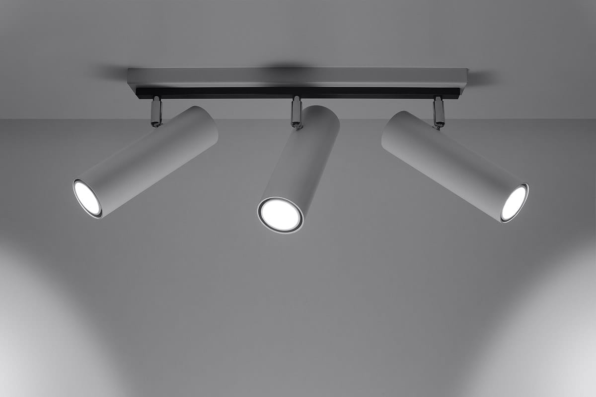 Trzypunktowa lampa sufitowa Direzione w kolorze białym, z cylindrycznymi kloszami skierowanymi w dół. Ułożona równolegle do sufitu, na prostokątnej podstawie. Klosze mają gładką fakturę i emitują jasne światło.