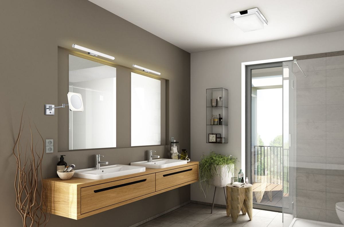 Kinkiet Mattimo LED w kolorze chromu, o wymiarach L60 cm i mocy 6,5W, zamontowany na ścianie w łazience. Posiada okrągłą głowicę, skierowaną na lustrzane odbicie. W otoczeniu drewnianej szafki z umywalką i nowoczesnym wystrojem wnętrza.
