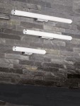Kinkiet LED Mattimo w kolorze chromu, o długości 80 cm i mocy 8,6W, z białym kloszem. Zainstalowany na szarej, kamiennej ścianie, ukazuje nowoczesny design z trzema równoległymi lampami. Idealny do oświetlenia wnętrz.