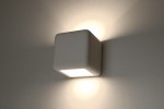 Kinkiet ceramiczny Nesta SL.0839 w białym kolorze, w formie sześcianu, zamontowany na ścianie. Emituje światło w górę i w dół, tworząc subtelny efekt oświetleniowy. Widoczna prostokątna powierzchnia na przedzie, bez dodatkowych zdobień.