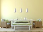 Lampa wisząca Gulcan 1-punktowa ceramiczna, w kolorze białym, zawieszona nad stołem w jadalni. Okrągły kształt, minimalistyczny design. Otoczenie: jasne ściany, drewniany stół, plecione krzesła z poduszkami w odcieniach zieleni.