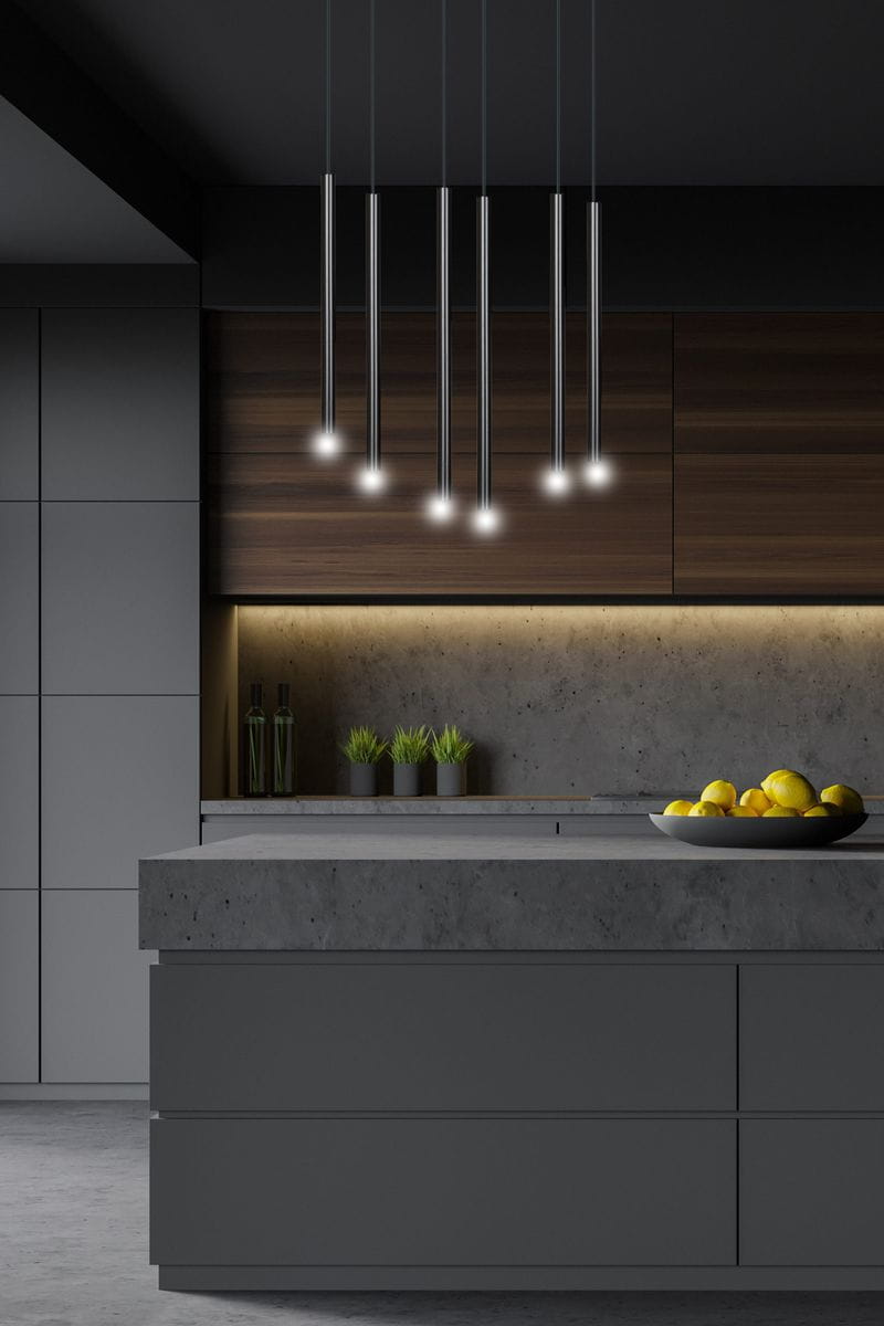 Lampa wisząca Selter, 6-punktowa, czarna. Składa się z sześciu cylindrycznych źródeł światła zawieszonych na cienkich linkach. Zainstalowana nad nowoczesnym blatem kuchennym, w tle drewniane szafki i szare ściany.