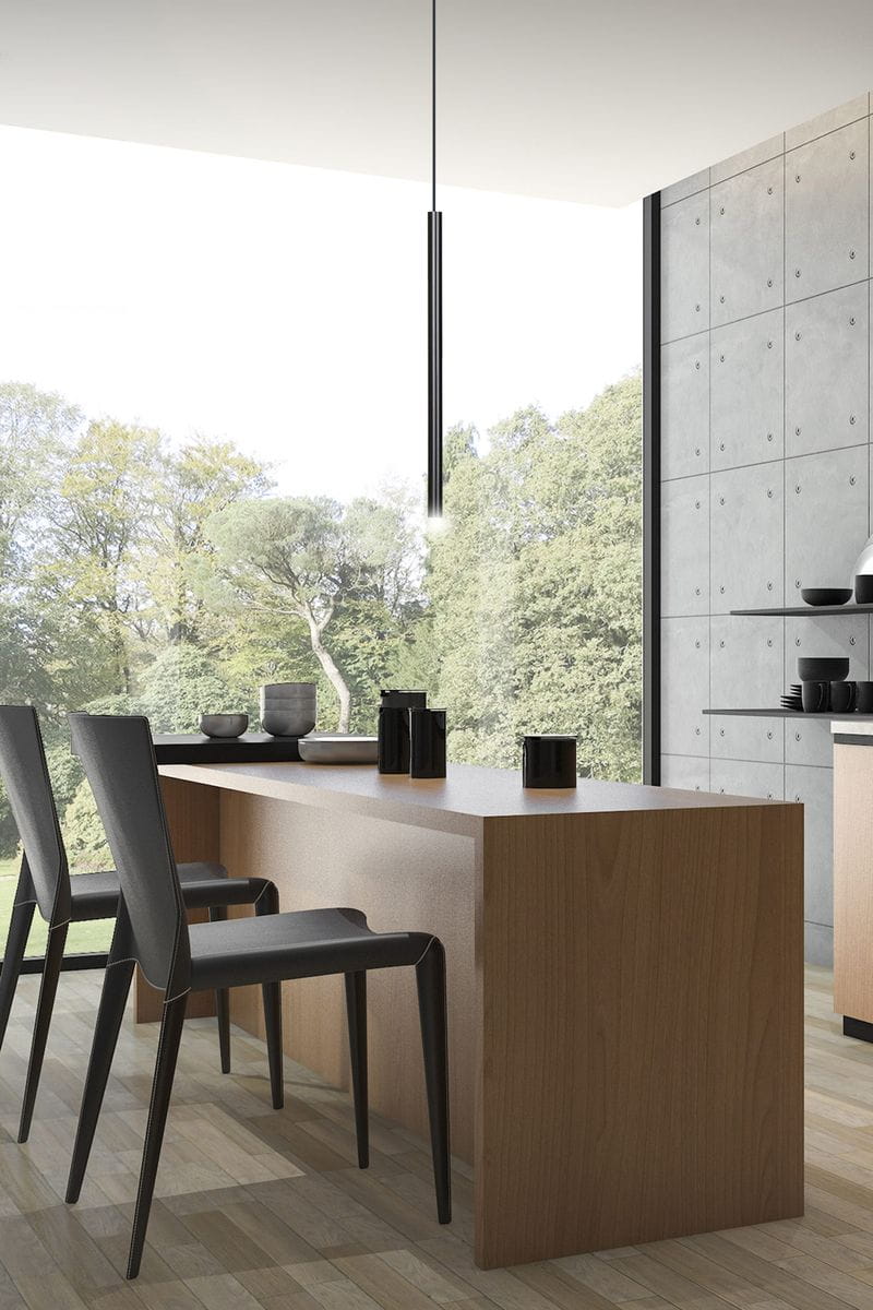 Lampa wisząca Selter 1-punktowa w kolorze czarnym, o smukłej, cylindrycznej formie, zwisająca z sufitu nad drewnianym blatem. W tle nowoczesne wnętrze z dużymi oknami i zielonym otoczeniem. Wysoka jakość wykonania, minimalistyczny design.