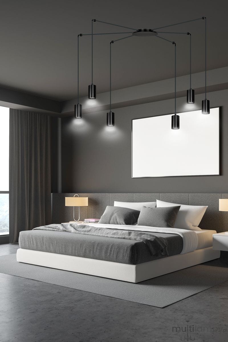 Lampa wisząca Traker 6-punktowa w kolorze czarnym, z sześcioma cylindrycznymi kloszami zawieszonymi na cienkich linkach. Ujęcie frontalne, zamontowana na suficie w nowoczesnej sypialni, z szarym łóżkiem i jasnymi lampkami nocnymi.