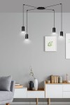 Czarna lampa wisząca Traker 4-punktowa z czterema cylindrycznymi kloszami zawieszonymi na cienkich linkach. Ujęcie z boku, lampa montowana do sufitu, w tle minimalistyczne wnętrze z szaro-białymi meblami i roślinami w doniczkach.