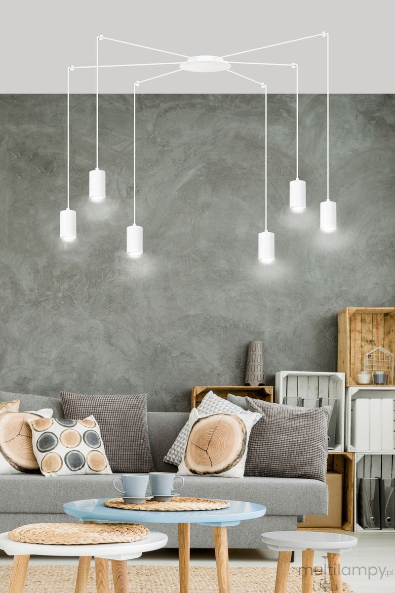 Lampa wisząca Traker 6-punktowa w kolorze białym, z sześcioma cylindrycznymi kloszami zawieszonymi na cienkich linkach. Produkt zamontowany na okrągłej podstawie, w aranżacji nowoczesnego salonu z szaro-beżowym tłem.