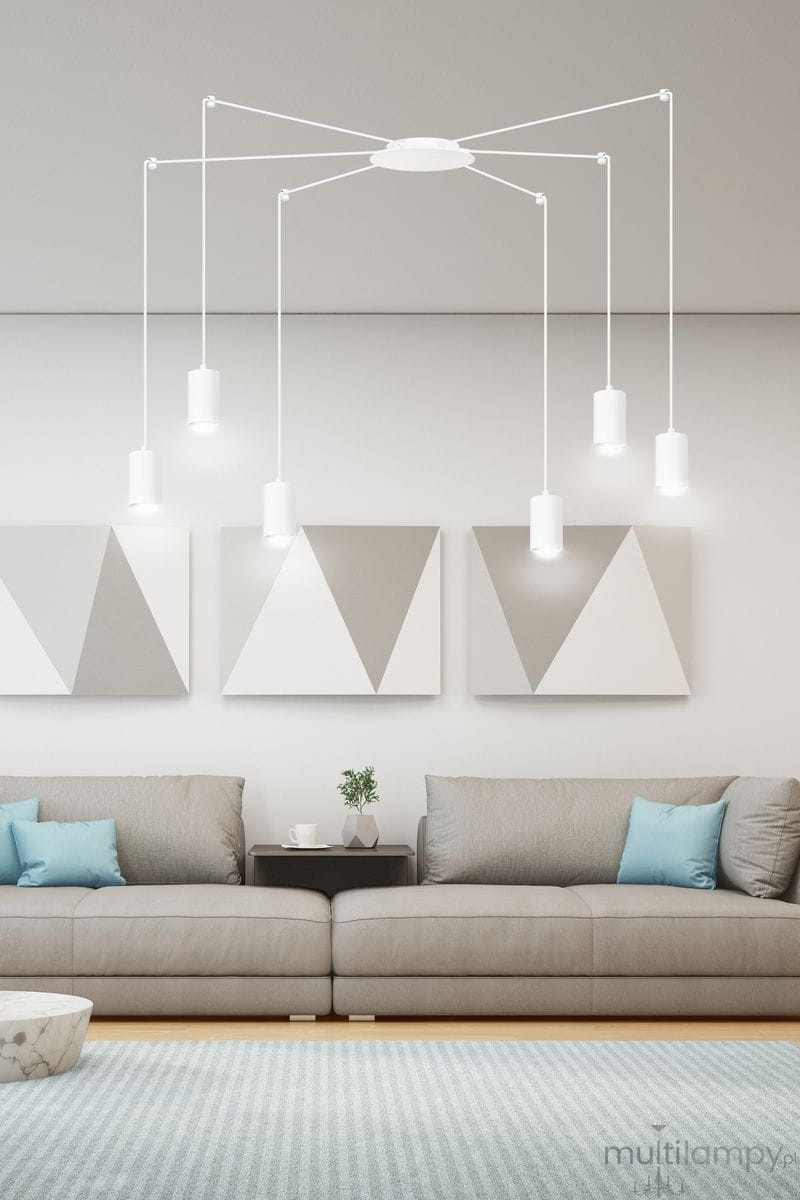 Lampa wisząca Traker 6-punktowa w kolorze białym z okrągłym stropem, sześcioma zawieszonymi oprawami w formie cylindrów. Zawieszona w nowoczesnym wnętrzu z szarymi grafikami na ścianach, nad szarym narożnikiem i stolikiem kawowym.
