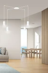 Biała lampa wisząca Traker 4-punktowa z cylindrycznymi kloszami, zawieszona na cienkich linkach. Ujęcie frontalne, pokazująca lampę w nowoczesnym wnętrzu z widokiem na morze. Klosze emitują światło, oświetlając strefę jadalnianą.