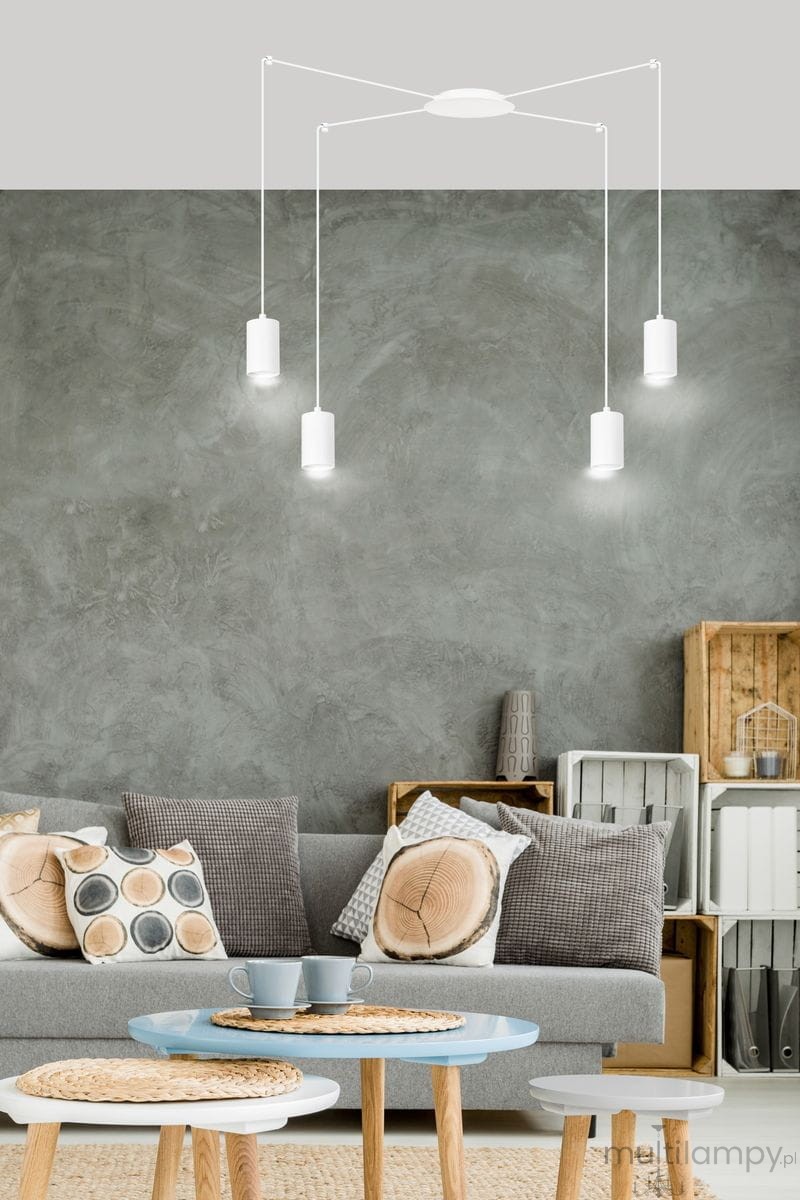 Lampa wisząca 4-punktowa Traker w kolorze białym, z czterema cylindrycznymi kloszami, zawieszona na cienkich linkach. Ujęcie z dołu, w kontekście nowoczesnego wnętrza z szarymi ścianami, kanapą i stolikami.
