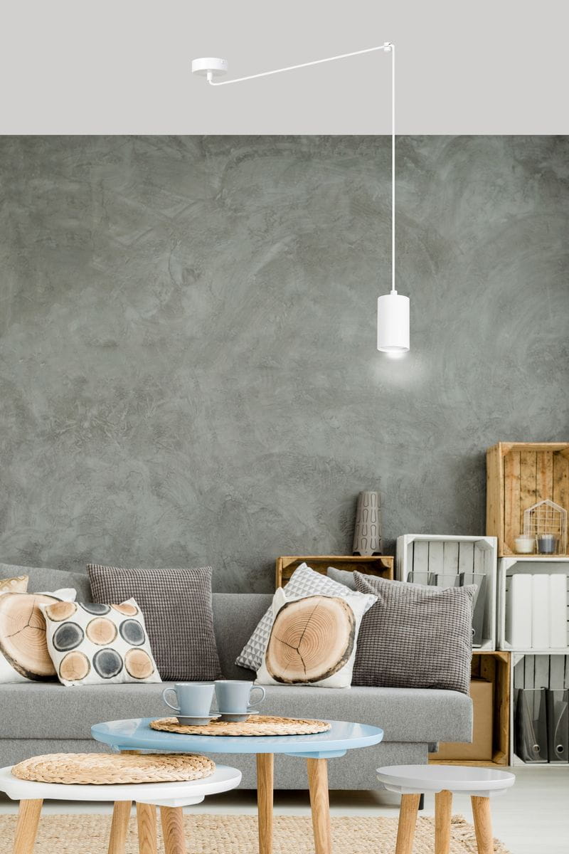 Lampa wisząca 1-punktowa Traker w kolorze białym, zawieszona na długim, prostym przewodzie. Produkt umieszczony w nowoczesnym wnętrzu z szarymi ścianami, obok sofy z poduszkami i stolików.