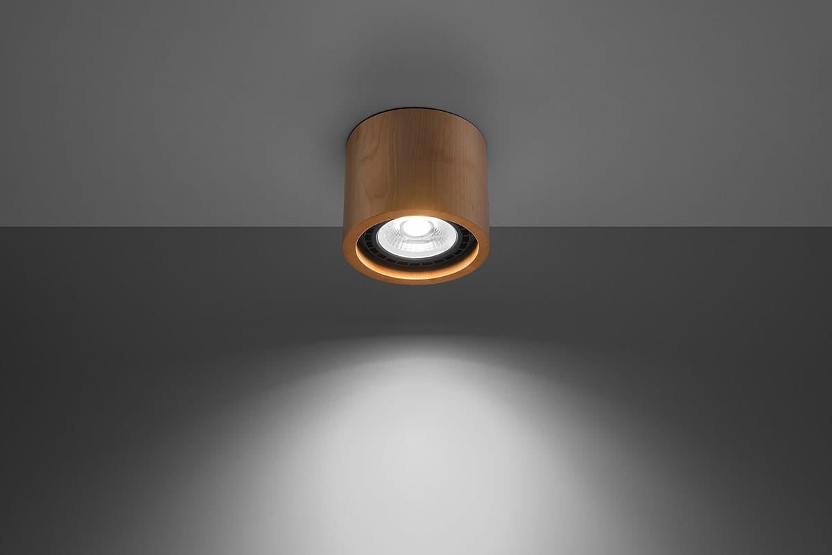 Lampa sufitowa 1-punktowa z drewna w kolorze jasnego drewna, zamontowana na szarym suficie. Okrągła obudowa z wykończeniem w naturalnym kolorze, z widoczną żarówką wewnątrz, emitująca światło w dół. Prosty, nowoczesny design.