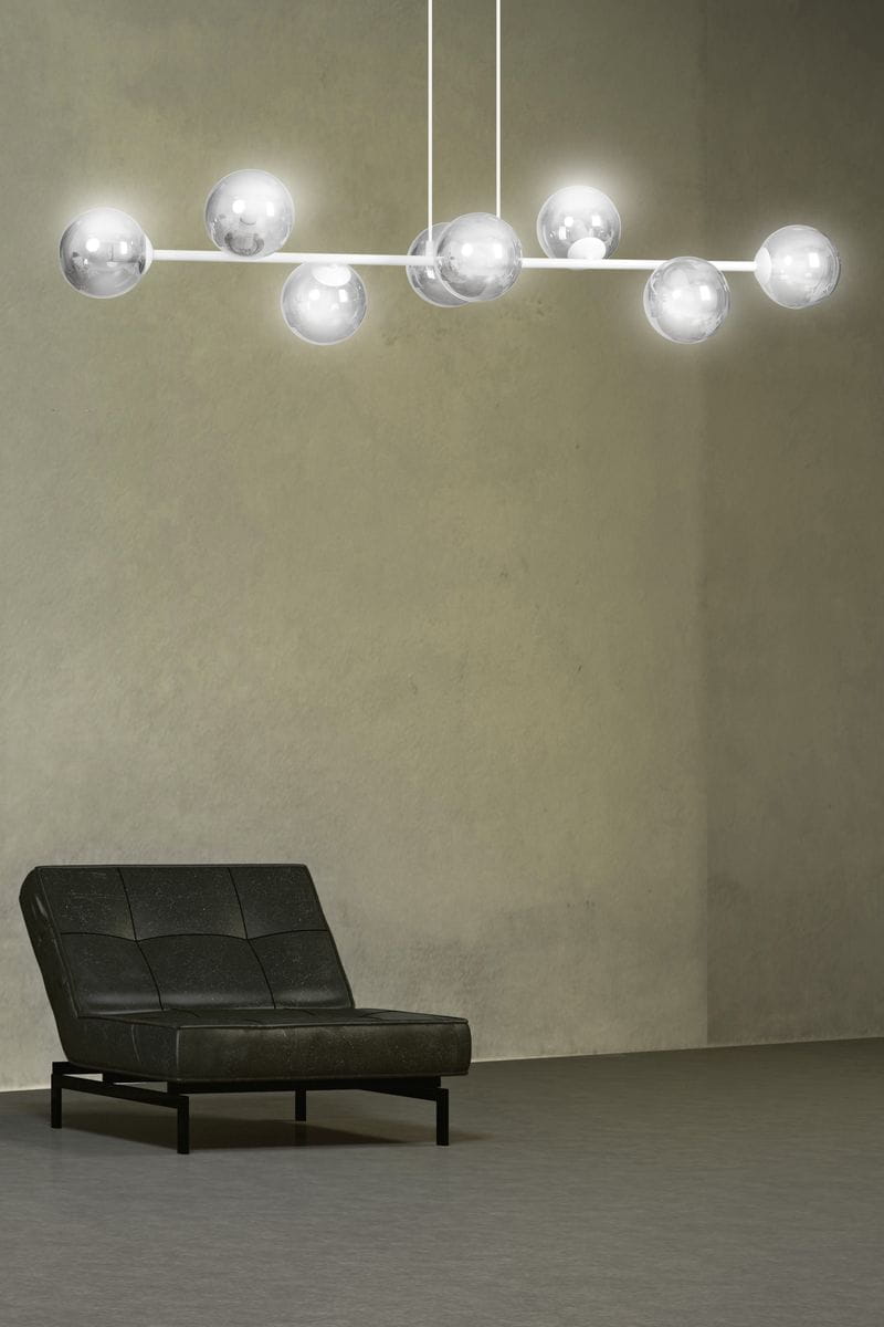 Lampa wisząca Rossi 8-punktowa w białym i grafitowym kolorze, zawieszona na dwóch cienkich kablach. Posiada osiem okrągłych kloszy z przezroczystego szkła, rozmieszczonych na prostokątnej ramie. Tło w neutralnym odcieniu, mebel obok w ciemnym kolorze.