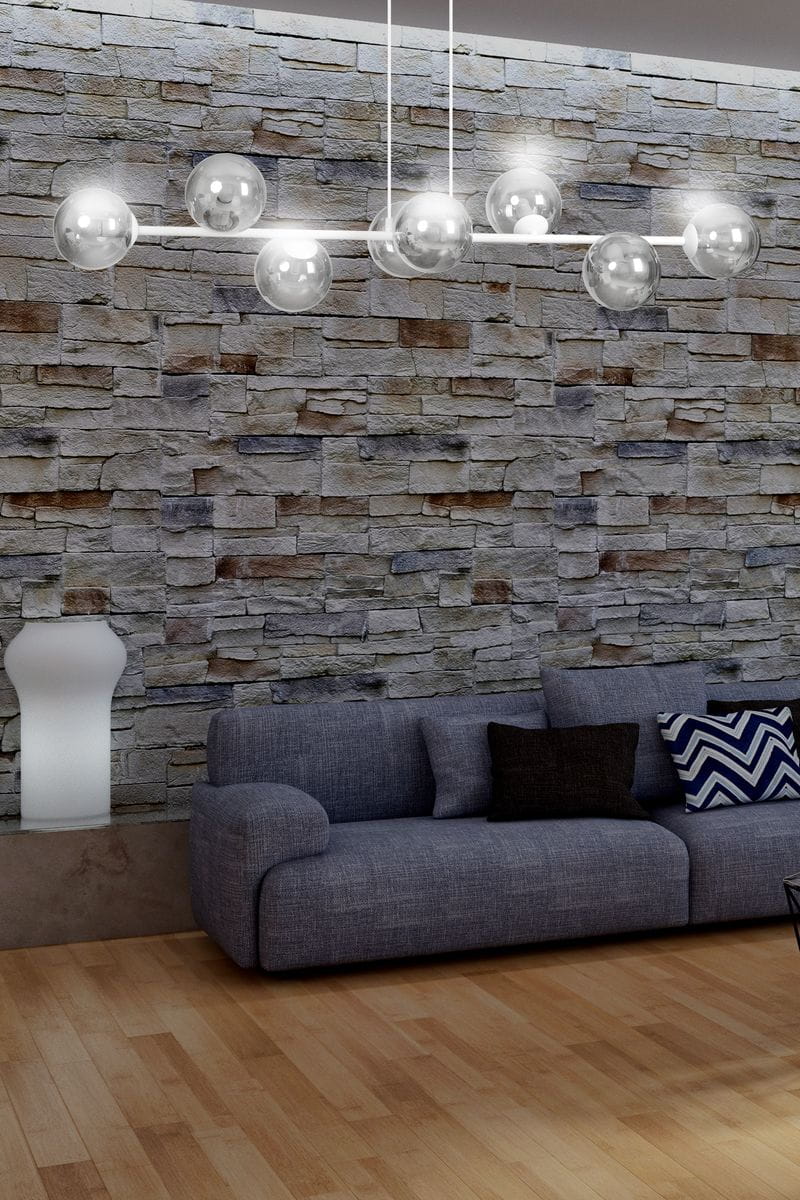 Lampa wisząca Rossi 8-punktowa w kolorze białym i grafitowym, z przezroczystymi kulistymi kloszami, zawieszona na cienkich, białych linkach. Widoczna w aranżacji z szarym sofą na tle kamiennej ściany.