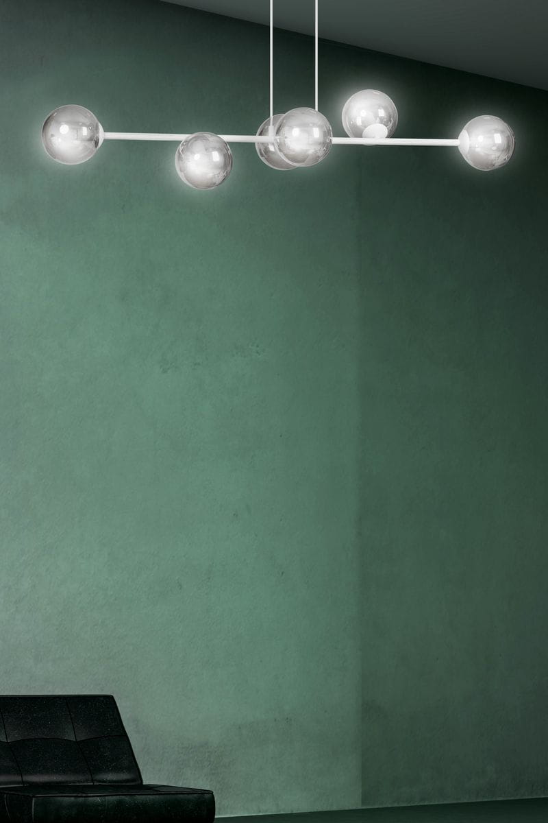 Lampa wisząca Rossi 6-punktowa w białym i grafitowym kolorze, z sześcioma przezroczystymi kulami, zawieszona na cienkiej białej rurce. Ujęcie frontalne, umiejscowiona w minimalistycznym wnętrzu z zielonym tłem.