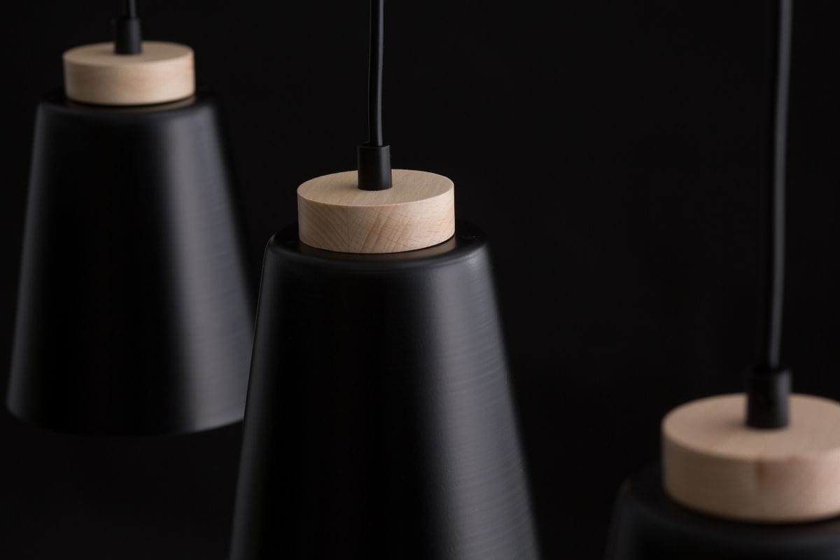Czarna lampa sufitowa (spot) 3-punktowa Atlas z metalowymi kloszami w kształcie stożków, zakończona drewnianymi elementami. Ujęcie z bliska, ukazujące detale mocowania i fakturę kloszy. Tło czarne, co podkreśla elegancki design lampy.