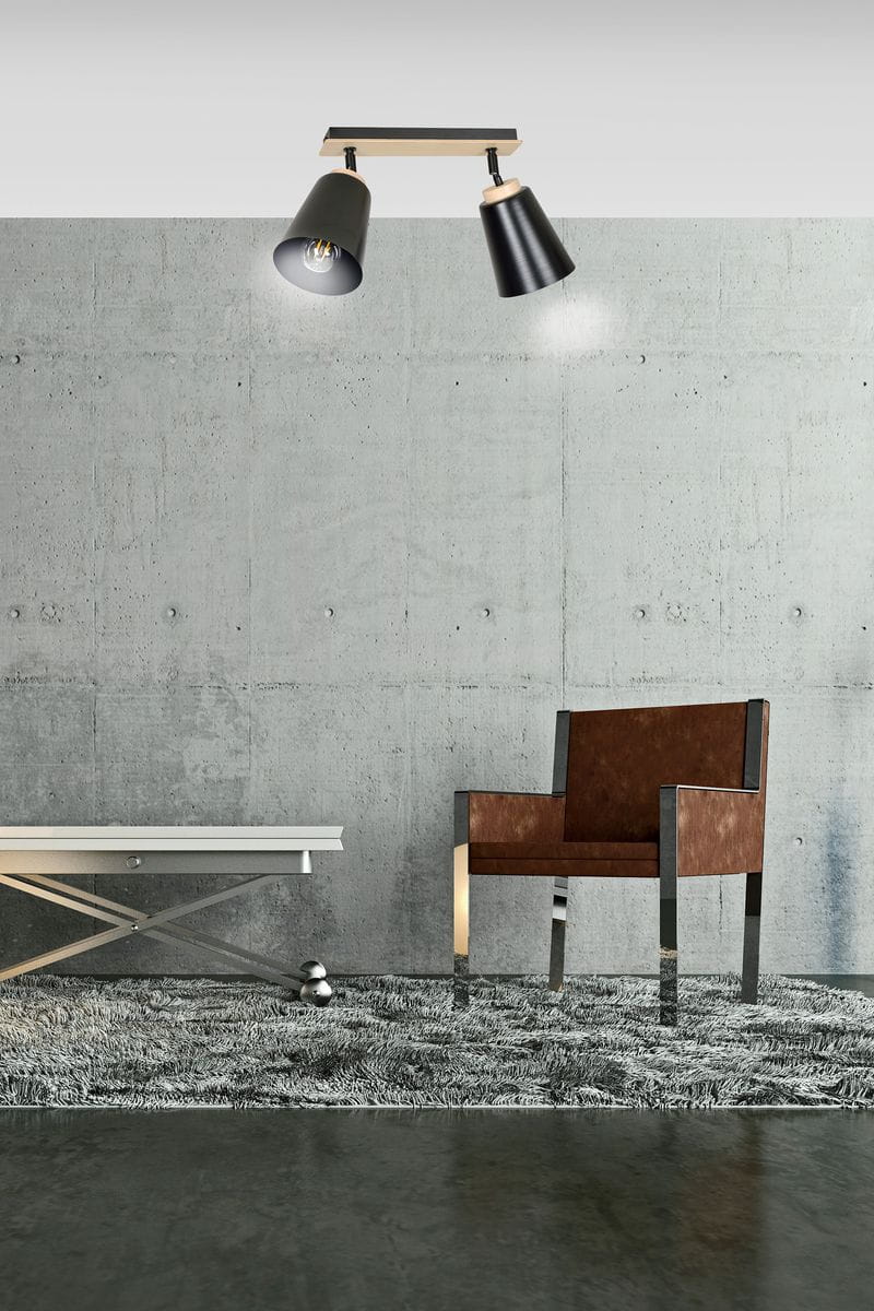 Czarna lampa sufitowa (spot) 2-punktowa Atlas z metalowymi kloszami w kształcie stożków, zamontowana na prostokątnej podstawie z drewna. Ujęcie z przodu, w nowoczesnym wnętrzu z betonową ścianą, fotelem i stolikiem.