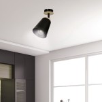 Czarna lampa sufitowa Atlas 1-punktowa w kształcie stożka, zawieszona na metalowym mocowaniu. Widoczna żarówka wewnątrz klosza. Produkt umieszczony w nowoczesnym wnętrzu z ciemnymi meblami i dużym oknem.