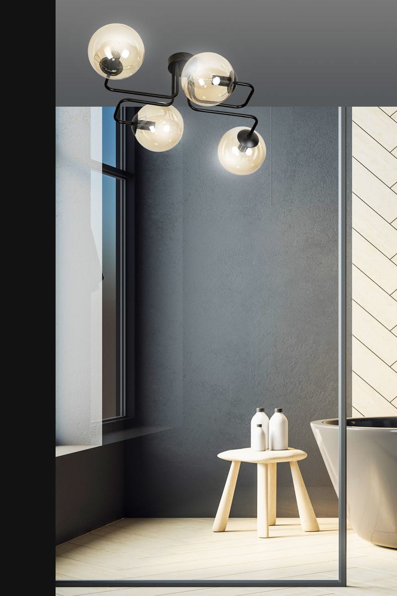 Lampa sufitowa Brendi 4-punktowa w kolorze miodowym. Konstrukcja z czarnymi elementami metalowymi, cztery szklane klosze w kształcie kul, zawieszone na elastycznych ramionach. Ujęcie z góry pokazujące lampę w nowoczesnym wnętrzu z oknem i stołkiem.