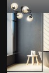 Lampa sufitowa Brendi 4-punktowa w kolorze miodowym. Konstrukcja z czarnymi elementami metalowymi, cztery szklane klosze w kształcie kul, zawieszone na elastycznych ramionach. Ujęcie z góry pokazujące lampę w nowoczesnym wnętrzu z oknem i stołkiem.