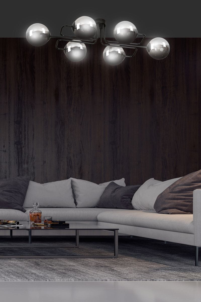 Lampa sufitowa Brendi A w kolorze grafitowym, z sześcioma okrągłymi kloszami, zamontowana na suficie. Widok z góry, w tle ciemne drewniane ściany i nowoczesny salon z szaro-białą sofą oraz niskim stołem.