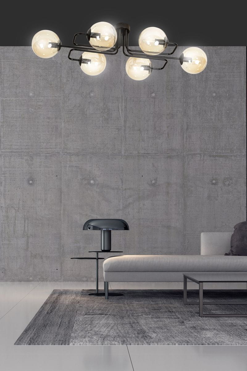 Lampa sufitowa Brendi A, sześciopunktowa, w kolorze miodowym. Posiada okrągłe klosze z przezroczystego szkła, zamontowana na czarnej konstrukcji. Widok z dołu, w nowoczesnym wnętrzu z szarym tłem i sofą.
