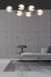 Lampa sufitowa Brendi A, sześciopunktowa, w kolorze miodowym. Posiada okrągłe klosze z przezroczystego szkła, zamontowana na czarnej konstrukcji. Widok z dołu, w nowoczesnym wnętrzu z szarym tłem i sofą.