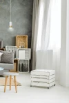 Lampa wisząca Fumiko 1-punktowa w kolorze białym z złotymi detalami, zawieszona na cienkim kablu. Widoczna w jasnym wnętrzu z szaro-białymi ścianami, obok mebli w stylu skandynawskim oraz drewnianymi skrzynkami.