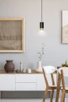 Lampa wisząca Fumiko 1-punktowa w kolorze czarnym z elementami złotymi, zawieszona na cienkim kablu. Produkt znajduje się w nowoczesnym wnętrzu, nad drewnianym stolikiem z dekoracjami, na jasnej ścianie.
