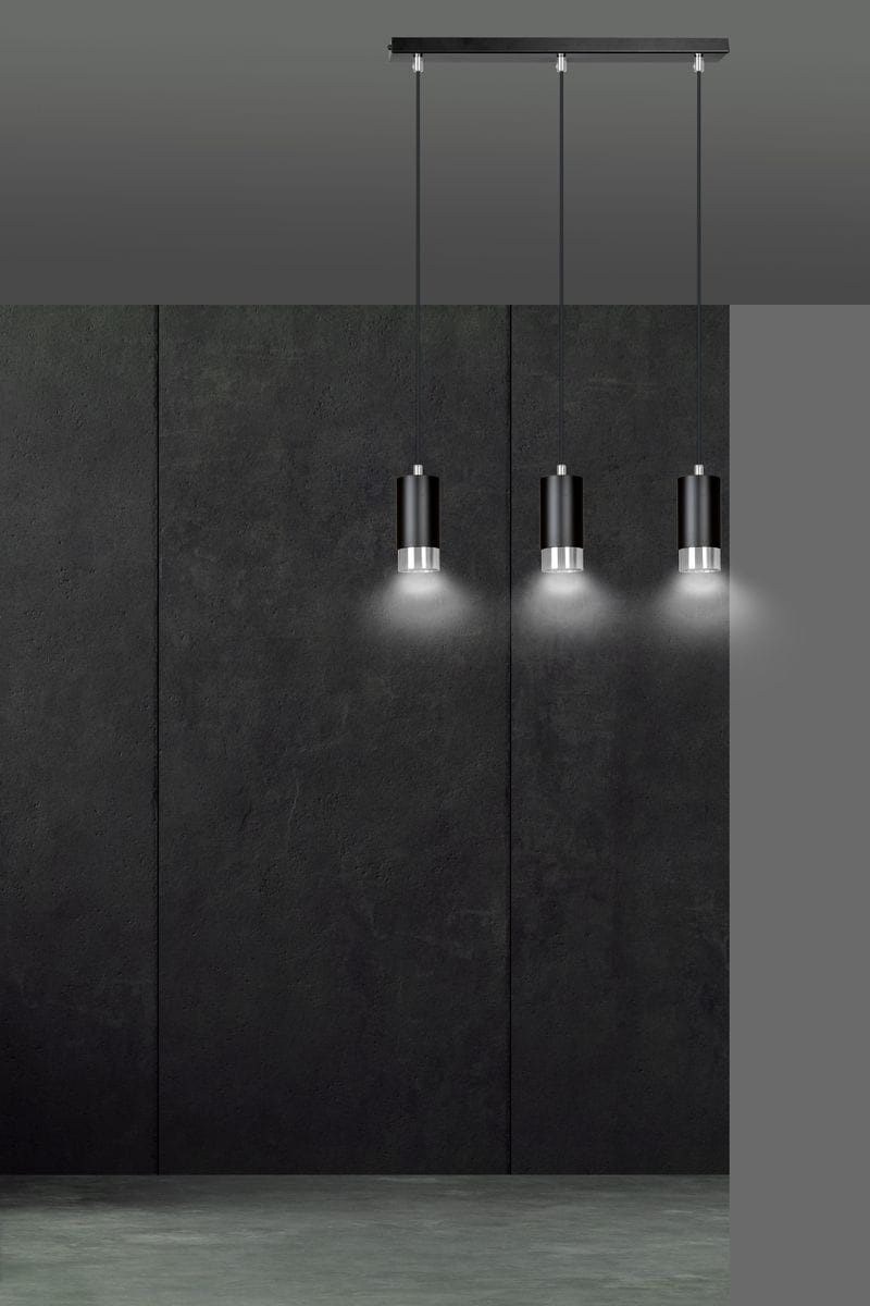 Lampa wisząca Fumiko 3-punktowa w kolorze czarnym z chromowanymi detalami. Posiada trzy cylindryczne klosze zawieszone na cienkich linkach. Ujęcie frontalne, produkt zamontowany na prostokątnej podstawie. Tło w odcieniach szarości.