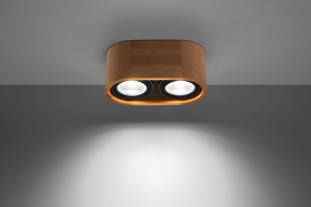 Lampa sufitowa 2-punktowa Basic wykonana z drewna, w kolorze naturalnym. Ma prostokątny kształt, z dwoma okrągłymi źródłami światła, zamontowana na szarym tle. Widoczne detale to gładka powierzchnia drewna oraz czarne elementy okrągłych reflektorów.