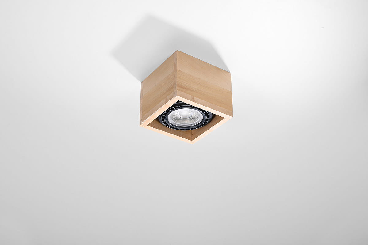 Lampa sufitowa Quatro 1-punktowa w kształcie sześcianu z drewna, w kolorze naturalnym. Ujęcie z dołu, pokazujące wnętrze lampy z żarówką, zamontowane na białym suficie. Brak widocznych napisów lub logo.