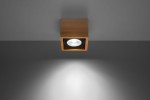Lampa sufitowa Quatro 1-punktowa w kolorze drewna, o kwadratowej formie. Zainstalowana na suficie, z widocznym reflektorem wewnętrznym. Oświetlenie rzuca jasne światło na szare tło.