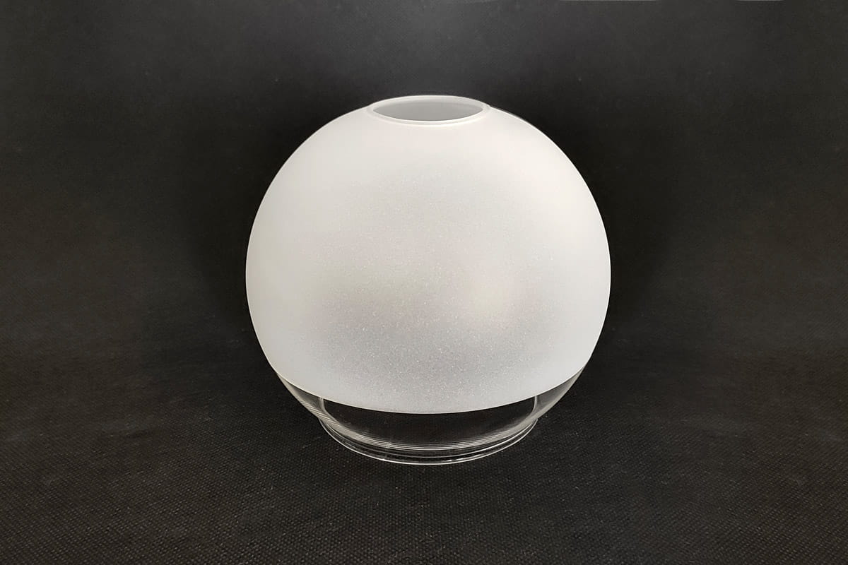 Klosz szklany w kształcie kuli, o średnicy 140 mm, matowy i transparentny, z górnym otworem. Ułożony na płaskiej powierzchni, z delikatną fakturą. Tło czarne, co podkreśla jego kształt i wykończenie.