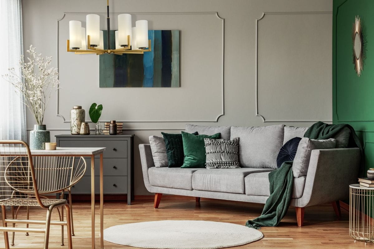Lampa wisząca Fortano MOD089PL-08BS z ośmioma punktami świetlnymi, w metalowej, złotej oprawie z białymi kloszami. Ujęcie frontalne, lampa zawieszona nad szarym sofą w nowoczesnym wnętrzu. W tle zielona ściana i dekoracje.