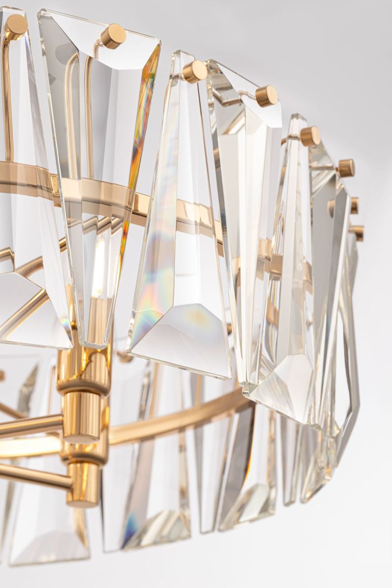 Lampa wisząca Puntes 6-punktowa w złotym wykończeniu. Szklane, wielokątne klosze refleksyjnie odbijają światło. Ujęcie z boku, blisko detali, ukazujące metalowy stelaż oraz elementy mocujące. Elegancka dekoracja do wnętrz.