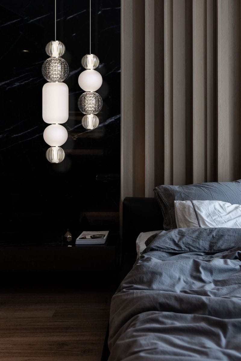 Lampa wisząca Collar LED w kolorze chromu, składająca się z okrągłych i owalnych elementów szklanych, w tym białych i przezroczystych kul. Zawieszona w pionie, w nowoczesnym wnętrzu z ciemnym tłem i drewnianymi akcentami.